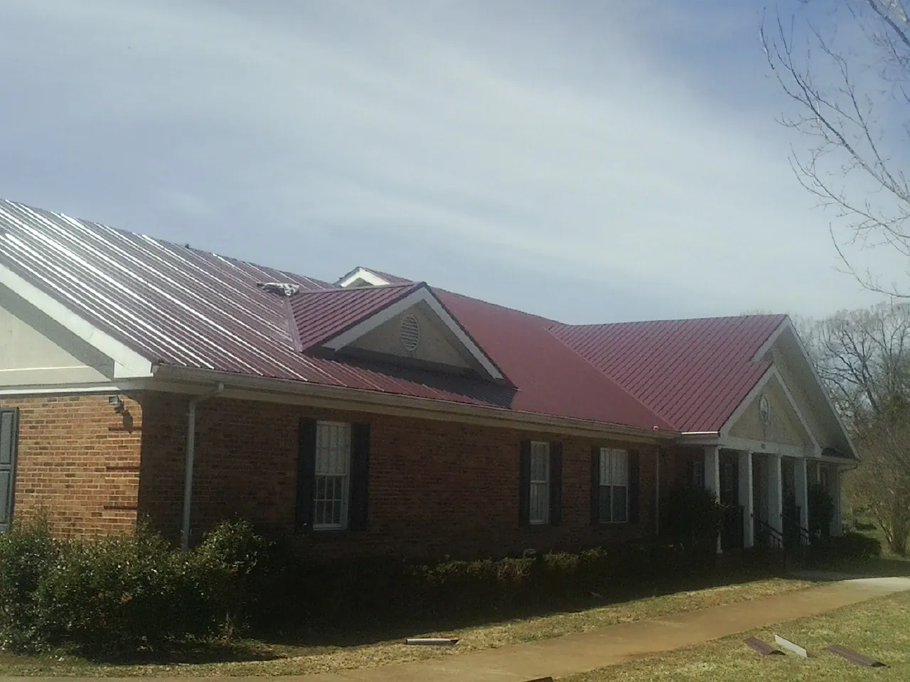 Red metal roof with gabled entries on a long brick building, from a Hail Damage Roof Repair job in Palos Park