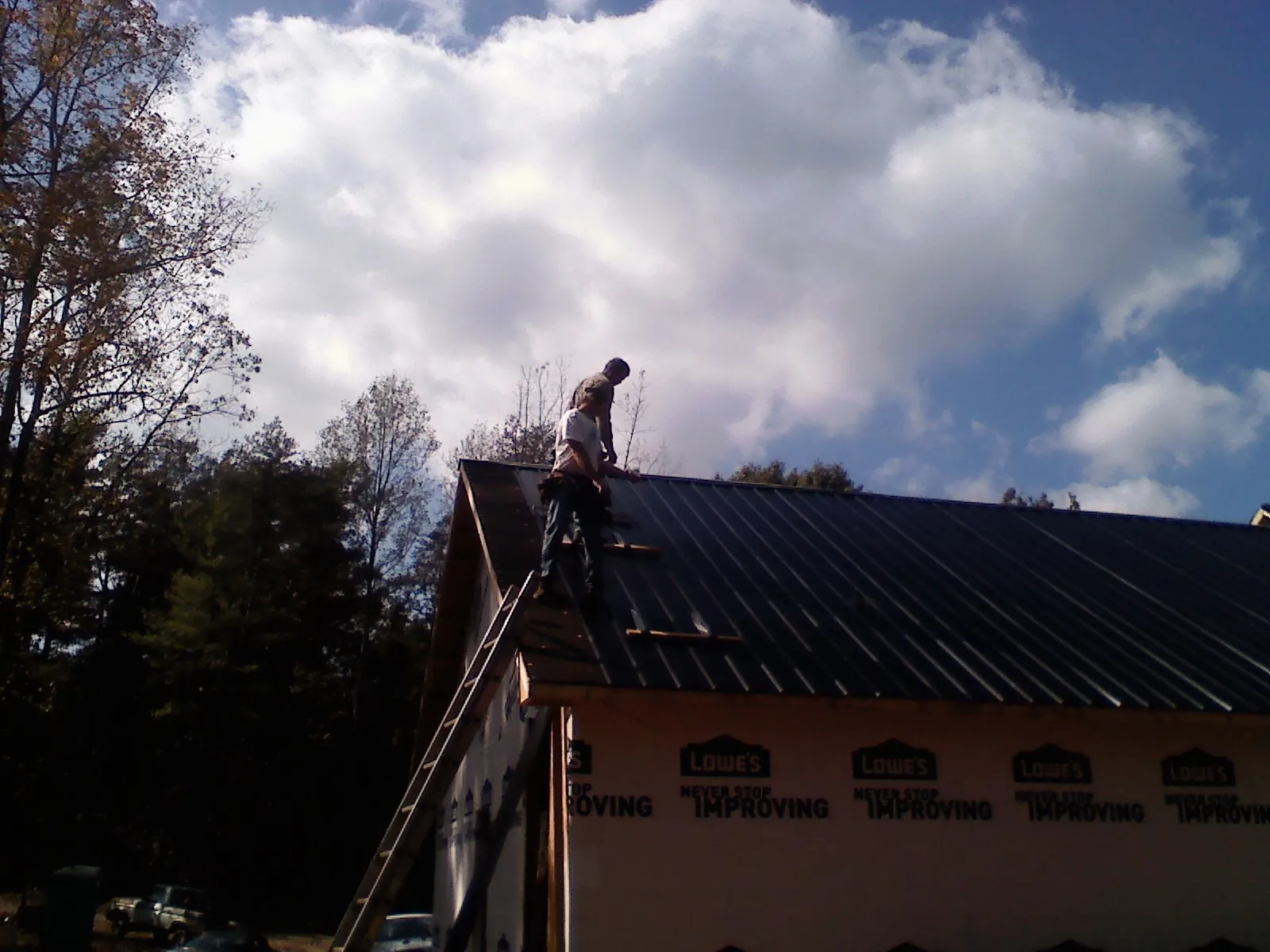 Roofer fastening dark metal panels high against a cloudy sky, from a Roof Inspection job in Palos Park