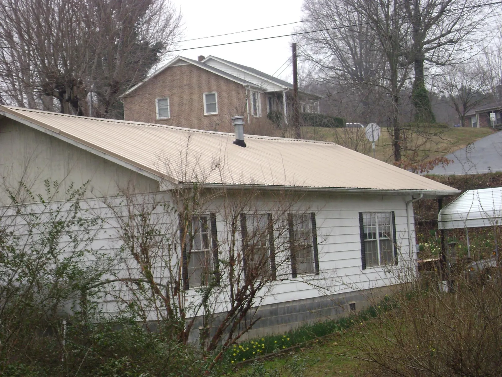Tan metal roof on a white sided house set into a hillside — Commercial Roofing by Roofing Brothers in Palos Park